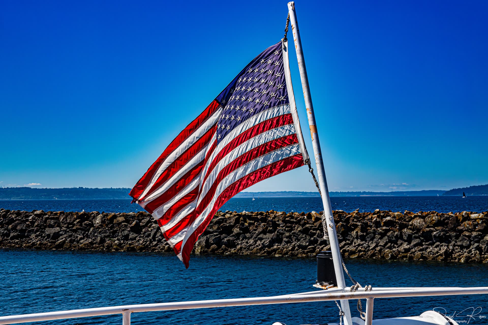 American flag flying above the breakwater under a clear blue sky.