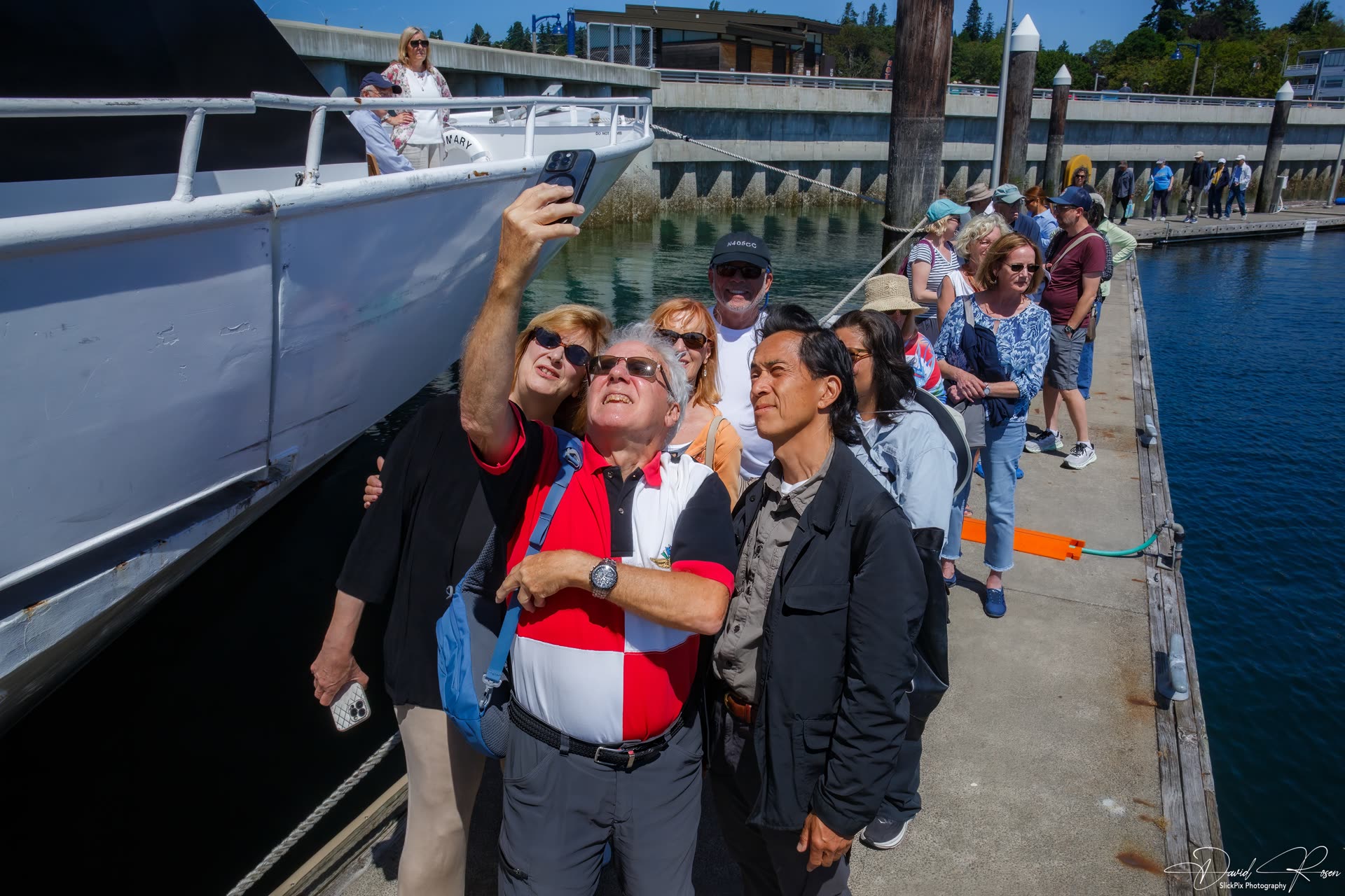 Passengers form a line along the dock next to the vessel.