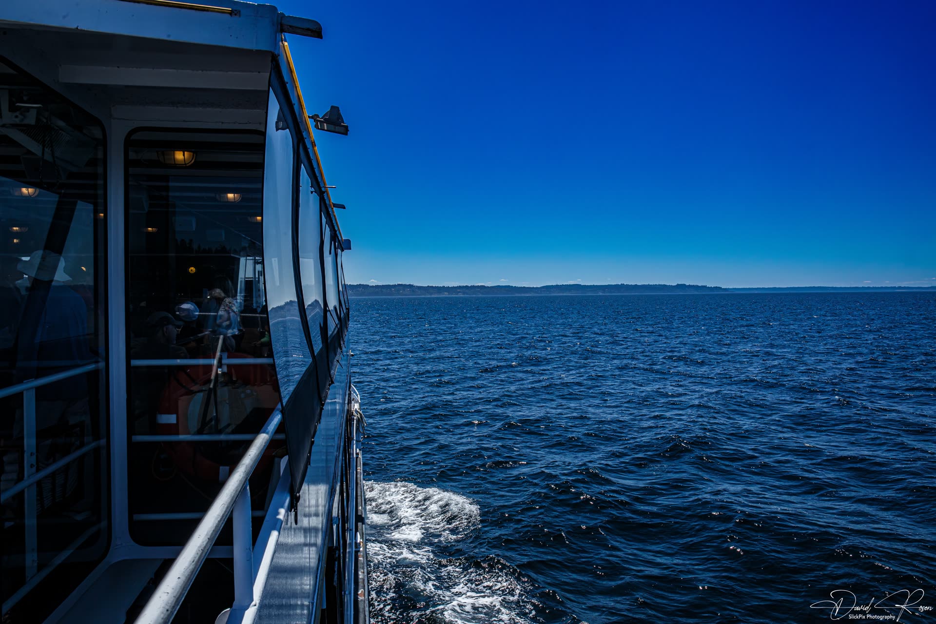 The vessel wake trails across dark blue water under a cloudless sky.