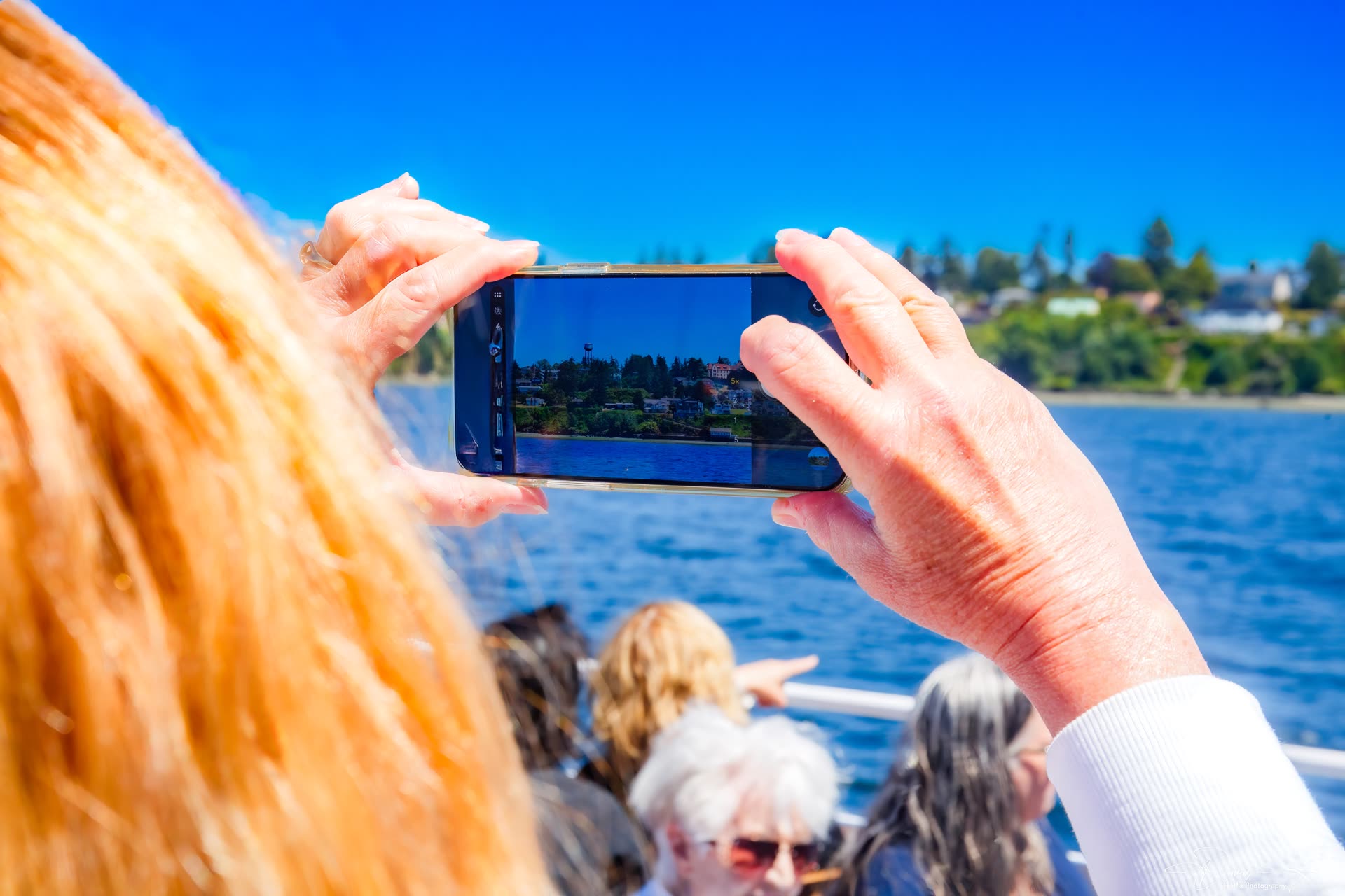 A passenger holds up a phone to photograph the shoreline.