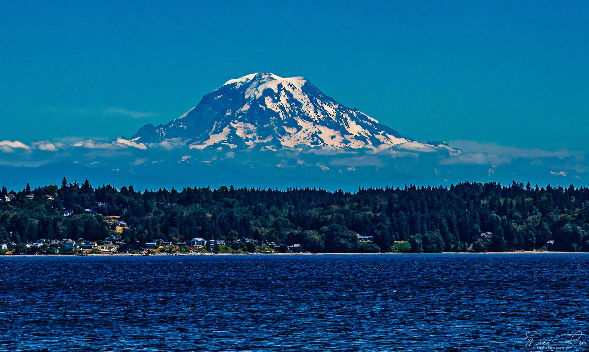 Telephoto view of snow-covered Mount Rainier above the distant shoreline.