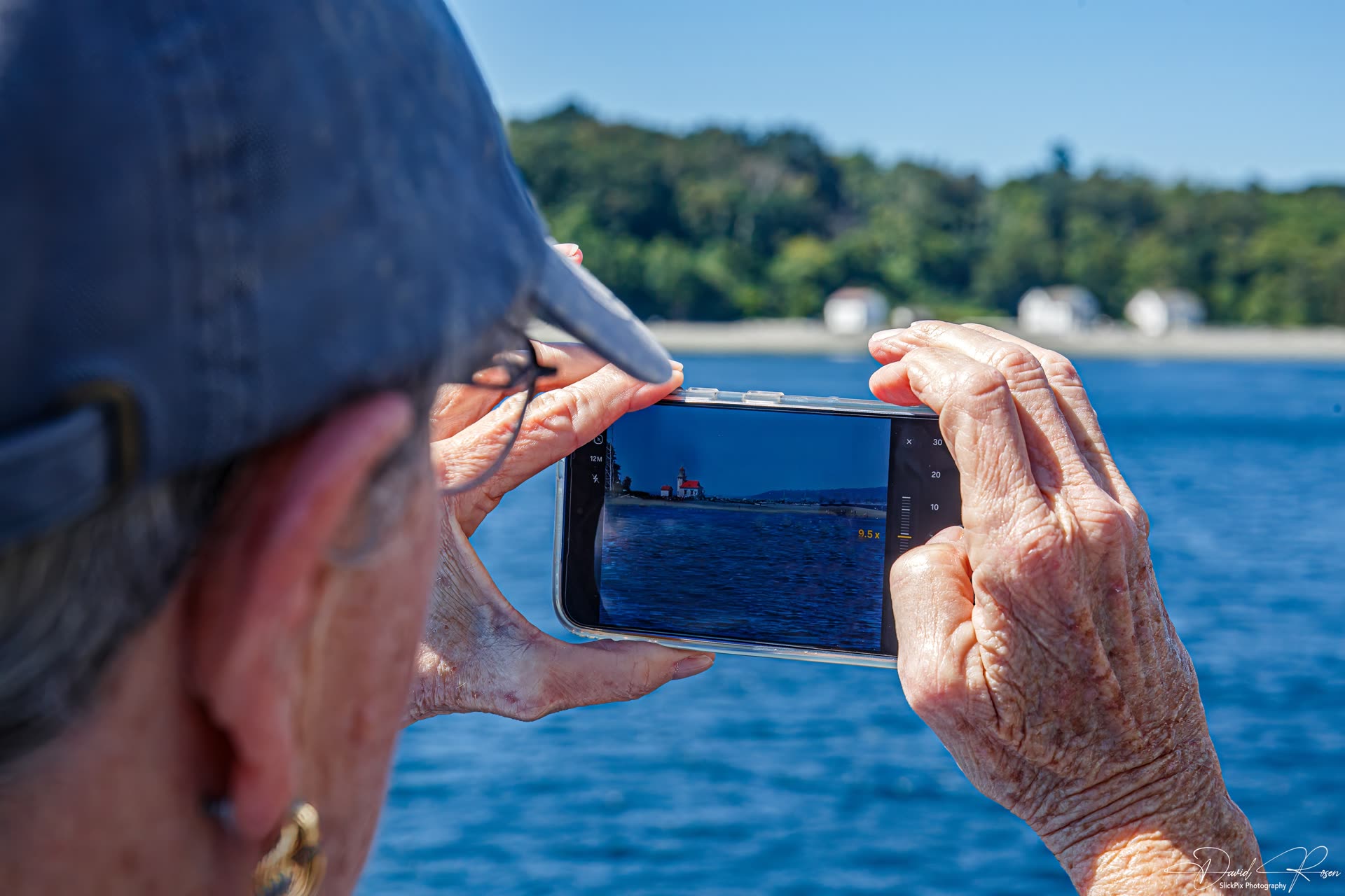 Close view of a passenger using a phone to photograph the shoreline.