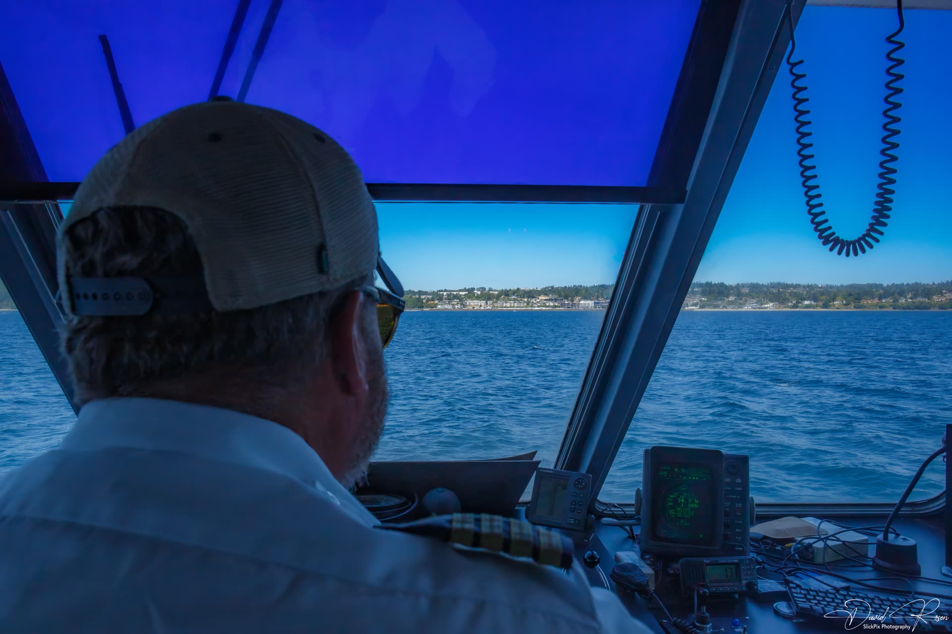 A crew member faces the wheelhouse windows while the vessel approaches shore.
